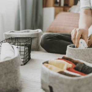 woman siting on bed puting clothes into organized bins